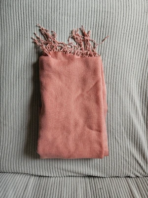 Ljusrosa sjal med fransar - En mjuk och stilren ljusrosa sjal med tunna fransar i ändarna. Perfekt att svepa runt halsen för en chill look. Materialet känns lent och lätt, och färgen är enkel att matcha med olika outfits. Används även som hijab huvudbonad. Själen är i bomullstyg 