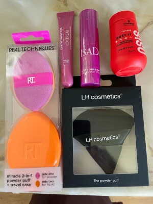 Makeup, tillbehör samt hårprodukt - Säljer två sminksvampar: en 2-i-1 powder puff från Real Techniques i lila och orange, samt en svart powder puff från LH cosmetics. Perfekta för applicering av puder och foundation. Båda har en mjuk, rundad form och är tillverkade i syntetiskt material. Isadora limpans cheek tint, läppglans samt en volympuder för håret. Nytt! Obrutna förpackningar.