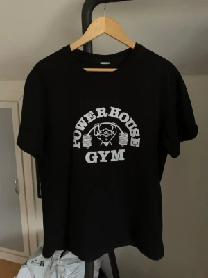 Svart Powerhouse Gym t-shirt - Säljer en svart t-shirt från Powerhouse Gym med vitt tryck framtill T-shirten är i 100% bomull och har en klassisk passform med korta ärmar och rund hals. Hör av dig vid minsta fundering och pris kan diskuteras! 😊💯