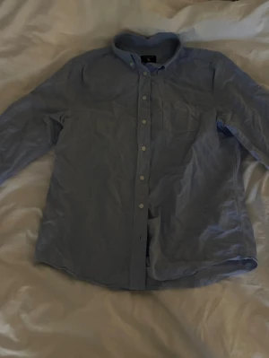 Ljusblå GANT skjorta - Klassisk ljusblå GANT skjorta med knappar framtill och bröstficka. Skjortan har lång ärm och button down-krage, perfekt för en clean och enkel stil. Passar till både jeans och chinos.