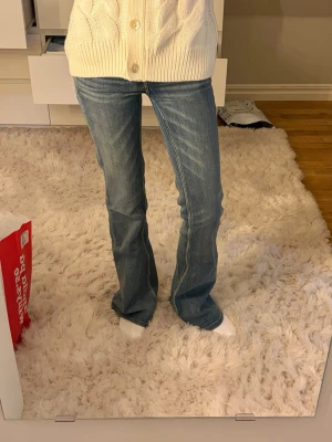 CheapMonday jeans - Säljer ett par blå bootcut jeans med snygga slitningar och ljusa detaljer. Jeansen har klassisk femficksdesign och låg midja. Perfekt för dig som gillar en avslappnad och trendig look. Materialet är denim och passformen är utsvängd nedtill. Lappen bak lite trasig, storlek 24/32