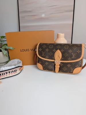 Iouis Vuitton Diane Monogram 🤎 - Exklusiv och mångsidig axelremsväska med sportig touch Investera i en tidlös ikon som kombinerar klassiskt hantverk med modern funktionalitet. Denna eleganta väska har en feminin, lätt rundad silhuett och erbjuder en perfekt balans mellan traditionell elegans och en samtida, sportig stil tack vare sin utbytbara rem. Detaljer och egenskaper: Material & Mönster: Slitstark, mörkbrun belagd canvas i det världsberömda, klassiska monogrammönstret. Kantad med vackra detaljer och förstärkta hörn i ljust