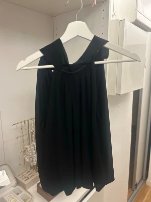 Svart ärmlös linnetopp - Snygg svart linnetopp med breda axelband och lös passform. Toppen har en enkel och stilren design som passar perfekt till många olika outfits. Tillverkad i ett mjukt och lätt material som känns skönt mot huden.