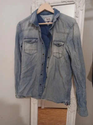 Ljusblå jeansjacka Hilfiger Denim - Säljer en ljusblå jeansjacka från Hilfiger Denim i klassisk modell. Jackan har två bröstfickor med lock och knappar framtill. Snygga sömdetaljer och en avslappnad passform gör den enkel att styla till olika looks.