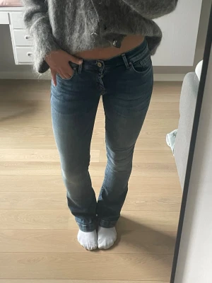 Blå LTB bootcut jeans med låg midja - Säljer ett par klassiska blå bootcut jeans med låg midja och lätt slitningar. Jeansen har fem fickor, knappgylf och är i stretchigt denimtyg som sitter snyggt på benen. Perfekta till en avslappnad look.