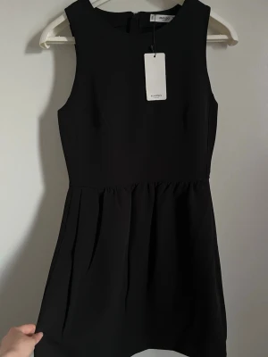Svart klänning från Mango - Stilren svart kortklänning från Mango i strl XS med rund halsringning och ärmlös design. Klänningen har en lätt utställd kjol och slät ovandel, perfekt för en enkel men elegant look. Tillverkad i ett mjukt material och är helt ny med prislapp. Köpt för 260 kr, säljer då den inte kommer till användning.