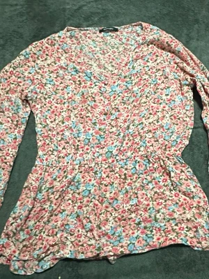 Blommig långärmad blus från Vero Moda - Söt blommig blus från Vero Moda med rosa, blå och vita små blommor. Blusen har v-ringning, lång ärm och markerad midja som ger en fin siluett. Tillverkad i ett lätt och mjukt tyg som känns skönt mot huden.