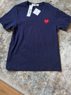 Blå Comme des Garçons PLAY t-shirt - Mörkblå t-shirt från Comme des Garçons PLAY med det ikoniska röda hjärtat med ögon broderat på bröstet. Klassisk passform, rund hals och korta ärmar. Tillverkad i mjuk bomull för en skön känsla.
