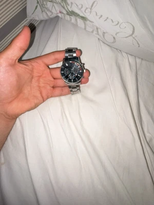 Stilren silverfärgad kronografklocka - Snygg kronografklocka med svart urtavla och detaljerade visare. Armbandet är i silverfärgad metall och klockan har flera små urtavlor för extra funktioner. Perfekt accessoar för dig som gillar en klassisk men modern look.