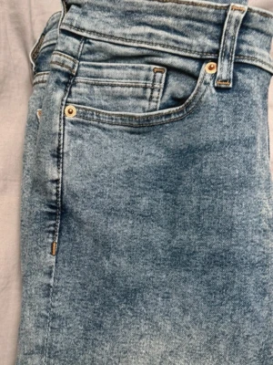 Ljusblå raka jeans - Säljer ett par ljusblå jeans med klassisk femficksmodell och raka ben. Jeansen har en tvättad look och detaljer i mässing vid fickorna. Perfekta för en avslappnad och trendig stil.
