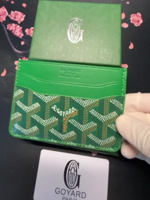 Grön korthållare - Snygg grön korthållare med det klassiska mönstret i vitt och gult. Tillverkad i canvas och läder, har flera fack för kort och en stilren design med Paris-logga. Perfekt för dig som vill ha något både lyxigt och praktiskt i fickan.