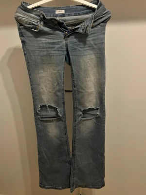 Blå slitna jeans  - Säljer ett par blå jeans från Nelly med slitningar och hål på båda knäna!