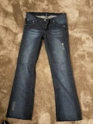 Victoria Beckham x Rock & Republic jeans - Snygga mörkblå jeans med raka ben och broderade kronor på bakfickorna. Jeansen har låg midja och råa kanter nertill för en edgy vibe. Tillverkade i klassiskt denim med slitningar framtill. Perfekta för dig som vill sticka ut lite extra. 🫶🏼Innerbenslängd : 71,5 cm Midja tvärs över : 37 cm
