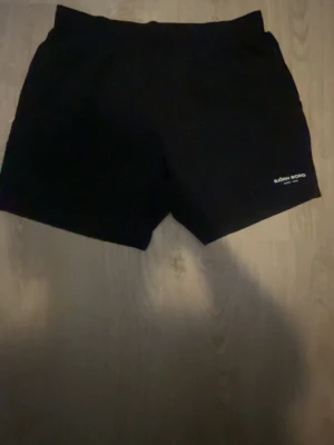 Svarta shorts från Björn Borg - Säljer ett par svarta shorts från Björn Borg med logotyp tryckt på benet. De har en enkel och klassisk design med elastisk midja och är perfekta för sport eller chill. Materialet känns mjukt och bekvämt, troligen bomull eller polyester.