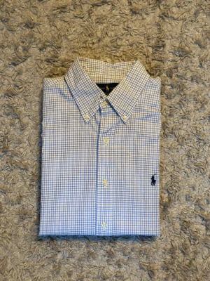 Blårutig skjorta från Ralph Lauren - Klassisk blårutig skjorta från Ralph Lauren med button-down krage och broderad logga på bröstet. Skjortan har långa ärmar och knäppning framtill. Tillverkad i mjuk bomull som känns skön mot huden. Perfekt för en clean och stilren look.