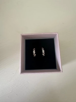 Edblad örhängen  - Säljer ett par silvriga örhängen med tvinnad design. De är små hoops i metall med en cool, vriden form som ger en modern touch till din stil. Perfekta för dig som gillar minimalistiska men ändå unika accessoarer. Helt ny och säljs för att jag har bytt till guld, pris kan diskuteras!🥰