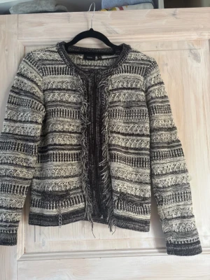 Mönstrad svartvit jacka/kofta - Säljer en svartvit kofta med coolt mönster och fransdetaljer och små kedjor längs öppningen och fickorna. Koftan har rund hals, långa ärmar och är stickad i ett mjukt material. Från det danska märket fransa i storlek S. Perfekt nu till sommaren!💞💞