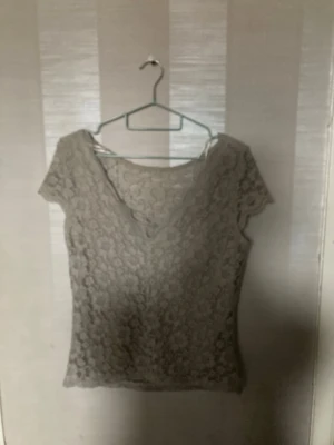 Beige spetsblus från VILA - Säljer en beige spetsblus från VILA med v-ringning och korta ärmar. Blusen har ett genomgående spetsmönster som ger en romantisk och feminin look. Perfekt att styla med jeans eller kjol för en trendig outfit.