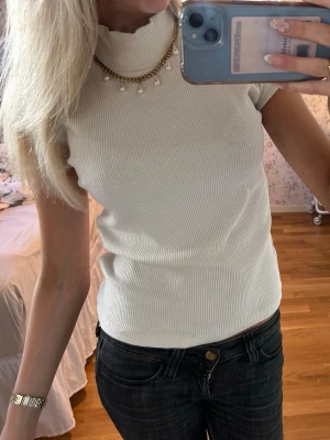 Vit ribbad polotopp - Säljer en vit ribbad polotopp med korta ärmar. Toppen har en krage och är tillverkad i ett stretchigt material som sitter snyggt mot kroppen. Perfekt att styla med jeans eller kjol för en clean look.