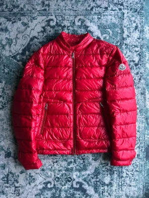 Röd dunjacka från Moncler - Snygg röd dunjacka från Moncler med quiltad design och två dragkedjeförsedda fickor framtill. Jackan har en klassisk Moncler-logga på ärmen och stängs med dragkedja. Perfekt för dig som vill ha en lätt och stilren jacka. ÄKTA! Med bevis, DUSTBAG INGÅR!!
