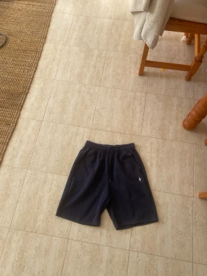 Marinblå shorts från Polo Ralph Lauren - Snygga marinblå shorts från Polo Ralph Lauren med elastisk midja och diskret logga broderad på benet. Perfekta för sommardagar och chill häng. Klassisk design och skön passform. Storlek S men passar Xs o M skulle jag säga. 
