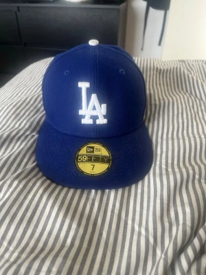 Blå LA-keps från New Era 59FIFTY - Snygg blå keps från New Era 59FIFTY med LA-logga broderad i vitt framtill och New Era-logga på sidan. Klassisk rak skärm och strukturerad passform. Perfekt för dig som gillar streetwear och sportig stil.