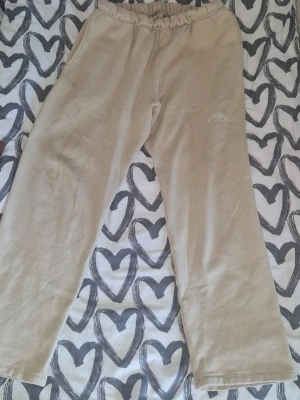 Beige mjukisbyxor Essentials - Säljer ett par beige mjukisbyxor från Essentials. Byxorna har en relaxed fit med resår i midjan och diskret logga broderad på låret. Perfekta för chill dagar och riktigt sköna tack vare det mjuka materialet. Snöret har bullat in sej.