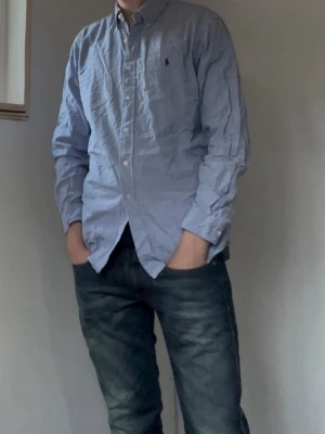 Ralph Lauren | Skjorta | L - Klassisk blårutig skjorta från Polo Ralph Lauren med button-down krage och broderad logga på bröstet. Skjortan har lång ärm, vita knappar och är tillverkad i bomull. Perfekt för en stilren look. Mått: 71 Längd, 52 Bredd
