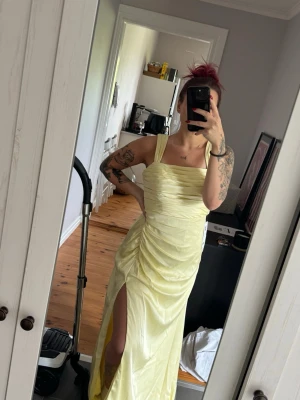 Ljusgul långklänning med slits från Azazie - Superfin citrongul klänning från Azazie! Perfekt nu inför bal och bröllop!  Säljer denna superfina klänning då de blev en annan modell för min del, så klänningen är endast testad!  Glidskydd på axlarna, både kedja och superfin  knytning i ryggen! Klänningen är satin stretch samt färg citrongul! Medföljer väska till klänningen så att den kan hänga i garderoben skyddad, eller ta med säkert på resa!  Skulle säga att strl är mer en större medium eller mindre large!  Ordinarie pris 1299:-