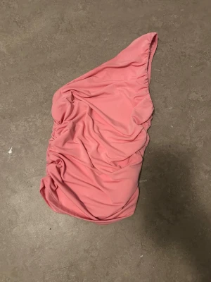 Rosa one shoulder baddräkt Pull&Bear - Trendig rosa baddräkt från Pull&Bear i one shoulder-modell. Tillverkad i mjukt, stretchigt material som sitter skönt på kroppen. Perfekt för dig som vill sticka ut på stranden med en modern och stilren look.