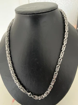 Kraftigt silverfärgat kedjehalsband - Snyggt halsband i silverfärgad metall med robust, fyrkantig kedjedesign. Länkarna är rektangulära och ger ett modernt, industriellt intryck. Perfekt för dig som gillar statement-smycken och vill ha något som sticker ut.
