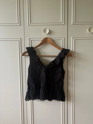 Svart volang topp med knyt - Snygg svart topp med volangdetaljer och knyt i ryggen. Säljer då den inte kommer till användning men är fortfarande i jättebra skick. Här även sytt in den lite för att den skulle passa mig men inte klippt så bara att sprätta upp