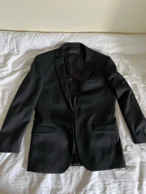 Svart slim fit kavaj Dressmann - En jättefin svart kavaj från dressmann. Den är i storlek 48 short slimfit vilket innebär att den ar lite kortare. Använd en gång.