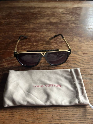 Louis Vuitton svarta och guldiga solglasögon - Snygga solglasögon från Louis Vuitton med svart och guldig båge samt mörka glas. Unik detalj med LV-logga. Perfekt för dig som vill höja din stil. DM för frågor eller funderingar 