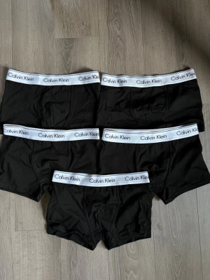 Svarta kalsonger från Calvin Klein - Fem par svarta boxerkalsonger från Calvin Klein med vit resår och logga runt midjan. Klassisk passform och stilren design, tillverkade i mjukt och stretchigt material för maximal komfort. ALDRIG använda!!!!