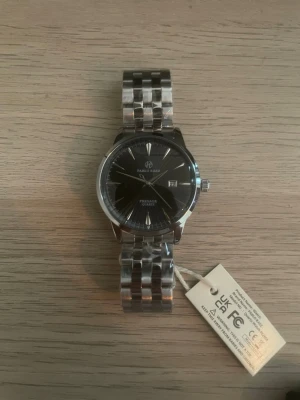 Silverfärgad klocka från Pablo Raez - Stilren klocka från Pablo Raez med svart urtavla och datumvisning. Armbandet är i blankt silverfärgat metall och har en klassisk länkdesign. Urtavlan har minimalistiska index och visare i silver. Perfekt accessoar för dig som gillar en clean look.
