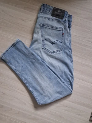 Ljusblå  jeans från Replay - Säljer ett par ljusblå skinny jeans från Replay med klassisk femficksdesign och snygga slitningar. Jeansen har en smal passform och är tillverkade i mjuk denim med stretch för extra komfort. Perfekta för en avslappnad och trendig look.