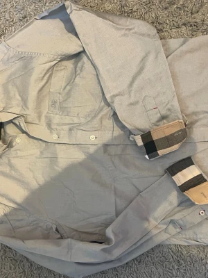 Ljusblå skjorta från Burberry Brit - Snygg ljusblå skjorta från Burberry Brit med klassiskt rutigt mönster på insidan av krage och manschetter. Skjortan är köpt på plick så kan inte garantera äktheten. Den är använd sparsamt och har inga synliga defekter vad jag kan se.