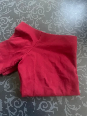 Röd off shoulder topp - Trendig röd off shoulder topp i mjukt bomullstyg. T-shirten har korta ärmar och en figurnära passform som framhäver axlarna. Perfekt för dig som vill ha en enkel men snygg topp till din garderob.