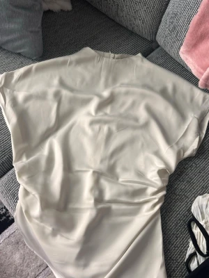 Ljusbeige sidenklänning med lös passform - Säljer en stilren ljusbeige klänning i siden med lös passform och ärmlös design. Klänningen har enkel rund halsringning och ett mjukt, glansigt material som ger en lyxig känsla. Perfekt för dig som gillar minimalistisk och elegant stil.