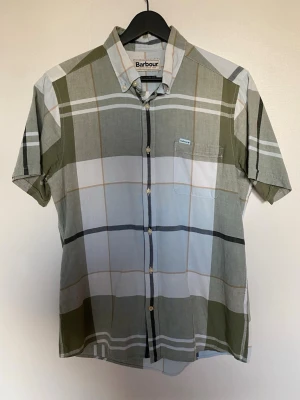Rutig kortärmad skjorta från Barbour - Snygg kortärmad skjorta från Barbour  i ett stort rutigt mönster. Materialblandnig: Bomull & Linne.  Knappt använd.        Bröstvidd: 50cm Längd:70cm