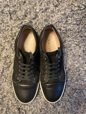 Svarta lanvin - Hej nu säljer jag min Stilrena svarta lanvin skor med ovandel i mocka och tåparti i slätt läder. Skorna har svarta skosnören, metallöljetter och vit sula som ger en clean kontrast. Perfekta för dig som gillar minimalistisk och lyxig streetstil.