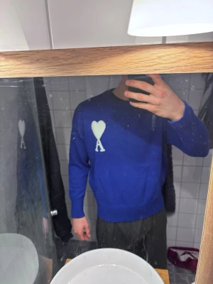 Blå stickad tröja från Ami Paris M - Snygg blå stickad tröja från Ami Paris med deras ikoniska vita hjärta och bokstaven A broderat på bröstet. Tröjan har rund hals, ribbade muddar och en avslappnad passform.