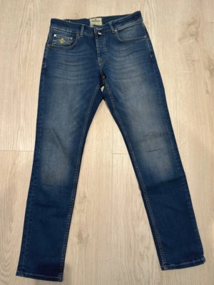 Blå jeans från Morris, rak modell - Säljer ett par klassiska blå jeans från Morris i rak modell. Jeansen har fem fickor, snygga slitningar och kontrastsömmar. Tillverkade i bomull med en skön passform. Sparsamt använda. Är 183 cm lång och bär storlek S/M. W30 L32. 