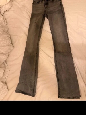 Grå raka jeans mid waist - Säljer ett par grå jeans med bootcut. Jeansen har klassisk femficksdesign och dragkedja med knapp. Materialet är denim i bomull och färgen är tvättad grå med lätt slitning. Perfekta till en avslappnad stil.