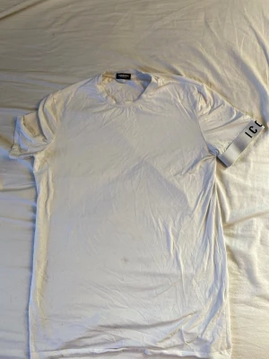 Vit t-shirt från Dsquared2 ICON - Vit t-shirt från Dsquared2 med trycket 'ICON' på ena ärmen. Klassisk rund halsringning och korta ärmar. Tillverkad i mjuk bomull för en skön känsla och stilren look.