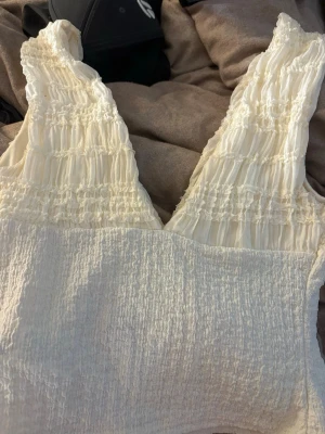 Vit smockad linnetopp -  Frakten betalar man själv.Supersöt vit linnetopp med smockad struktur och breda axelband. Toppen har en lätt rynkad design upptill och är ärmlös, perfekt för varma dagar. Materialet känns mjukt och luftigt, vilket gör den skön att bära. Enkel att matcha med jeans eller kjol.