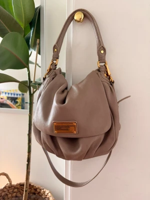 Vintage Marc Jacobs väska med guld detaljer - Vintage Marc Jacobs väska i mycket fint skick med guldiga detaljer😍😍Classic Q modell.  Både axelband och handtag!!  100% läder, går att justera axelbandet. Slukar mycket och väldigt smidig, passar till allt då det är en neutral färg💕
