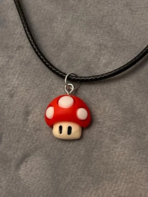 Super Mushroom Halsband Super Mario Smycke Nintendo Choker - Supersvampen från Super Mario som halssmycke! 🍄 Trädd på svart tråd, justerbar 40-45 cm. Berlocken är ca 1,6 x 1,6 cm. Perfekt för den som älskar Nintendo och mushroom kingdom.