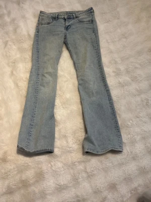 Ljusblå bootcut jeans - Säljer ett par ljusblå bootcut jeans med klassisk femficksdesign och normal midja. Jeansen har utsvängda ben och är gjorda i mjuk denim med bälteshällor. Perfekta för en avslappnad och trendig look.